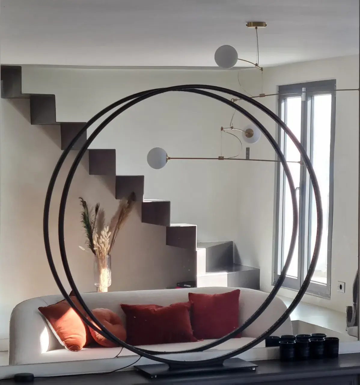 Salon du projet Lavoisier — double anneau de métal noir devant l'escalier suspendu en béton