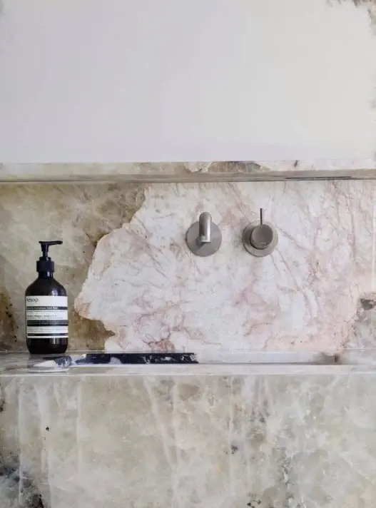 Salle d'eau sur mesure — vasque et crédence taillées dans un quartzite rosé translucide, mitigeurs encastrés en inox brossé